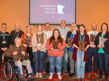 Group shot of people holding awards. Behind them is a screen with a slide saying Minnesota History Awards