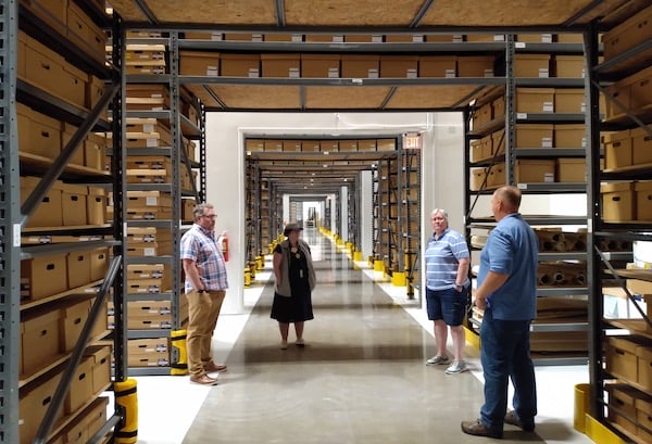 Four people standing in a hallway of the MNHS archives shelving and boxes surround them.