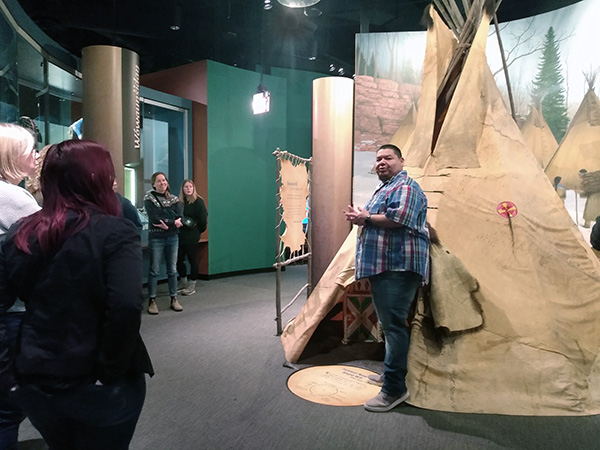 Guide giving tour of Hocokata Ti exhibit. Man standing next to teepee exhibit