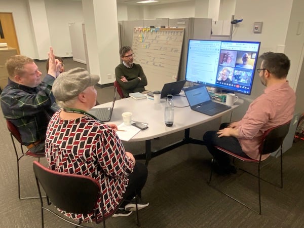Team Meeting with four people at table talking to three people on a computer screen