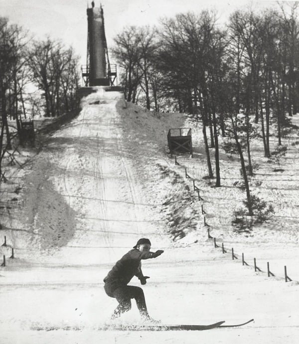 -Ski Jump in background with Man in foreground finishing jump 