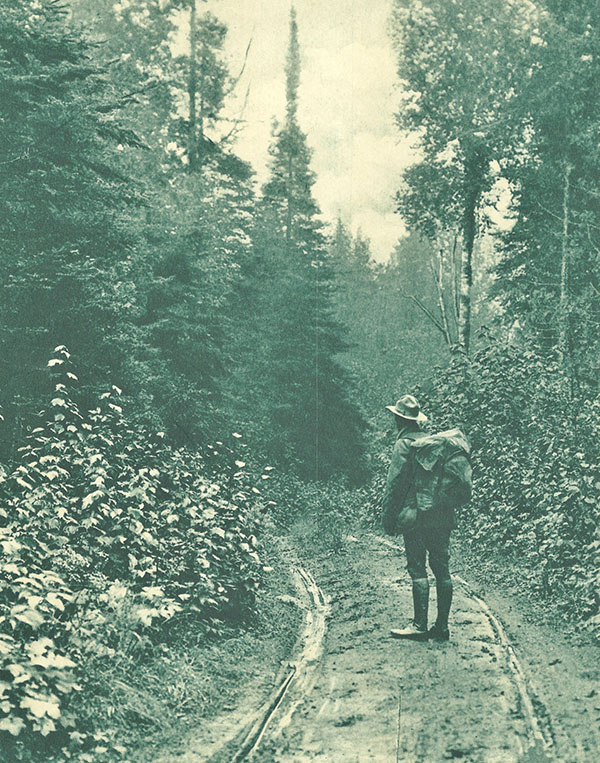 Gunflint Trail in 1917. Forest ranger standing on muddy road-trail with pack