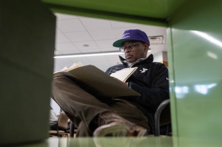 African American man in baseball cap reading files. YMCA logo is on his jacket