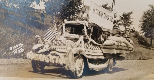 Float. Truck decked out in stars and stripes decrorations with banner saying My Country tis for thee. In the bed of truck are solders with rifles behind sandbags