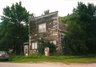 Butternut Store-Building with paint peeled off and trees and weeds growing around it