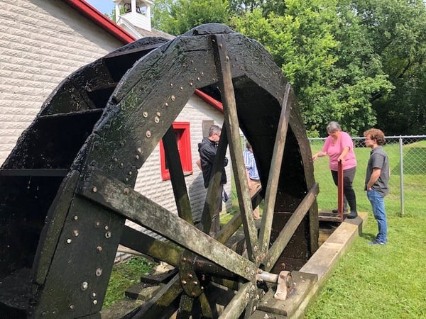 Four people standing around and inspecting the Morristown Feed Mill wheel