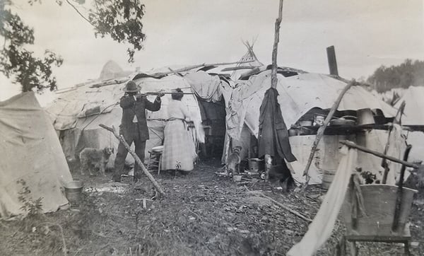 White Earth Native Americans and their homes. Native American man aiming gun off photograph. Native American woman behind him