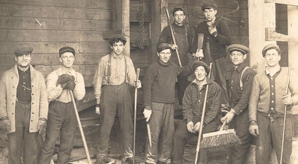 Nine men standing posing for picture with ice harvesting tools