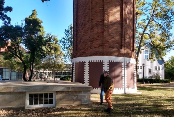 Man in hat standing on grass looking at concret plaform with brick water tower in background