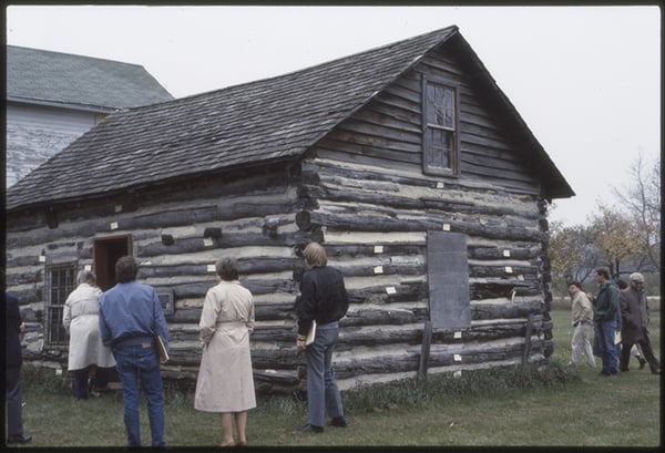 Several people walking around and looking at a log cabin