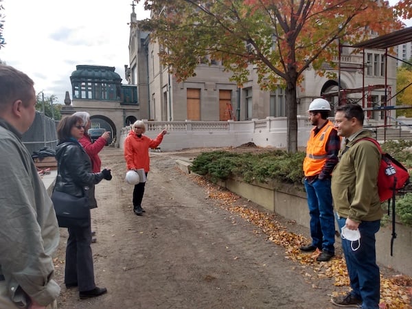 Five people standing in driveway of  Turnblad Mansion. Many of  the mansion's windows are boarded up. Scaffolding is off to the right of the photo. 