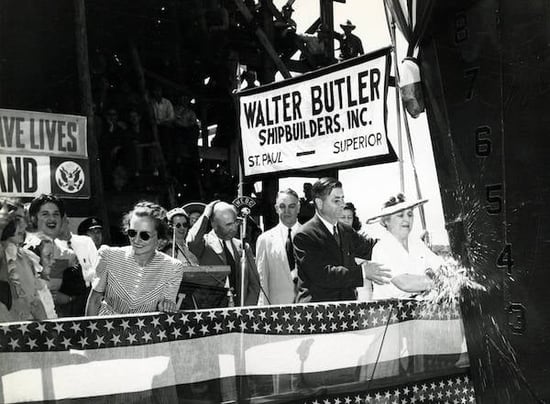 A woman breaks a bottle of champagne over the bow of a World War II Liberty ship