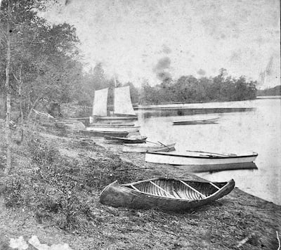 The photo in question. Grainy black and white photo showing lake shore with several boats (nine?). A canoe is in the foreground and a boat with sails in the distance.