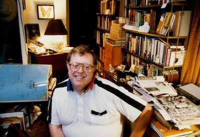 Photo of Jean Tretter at desk in his home with collection around him. ca 1990s