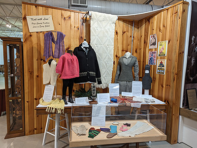 Photo of a display in the Knitting with Love exhibit showing mannequins and a display case with knitted items.