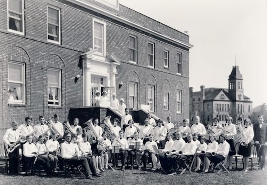 36 Brass band members sitting in chairs outside a hospital building Possibly high school students. Nurses standing on steps