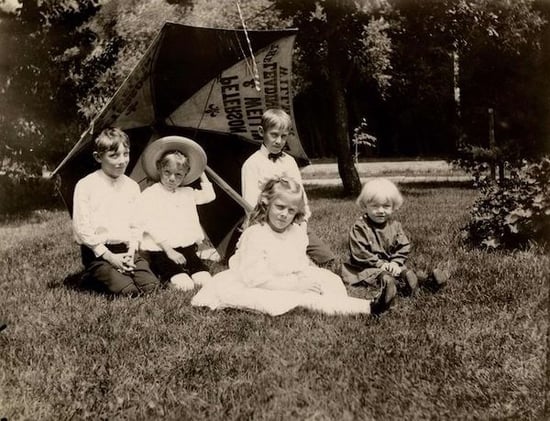 Five children on the courthouse lawn holding a umbrella advertising the Peterson and Wellin General Store