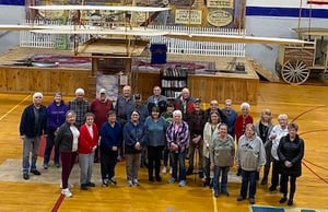 25 Pine County History Museum volunteers are standing in the middle of the gallery floor looking up at the camera