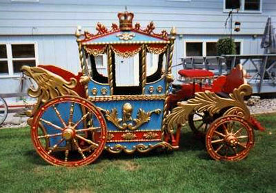 A very colorful old-timey circus wagon stage coach painted red, blue and gold. Decorative carvings are adoring the wagon with an eagle head at the wagons rear