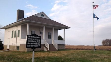 Exterior of the District 6 School building. Historic Marker sign is in the foreground and a farm field is in the background