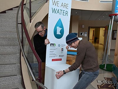 Two men installing We are water mn exhibit display