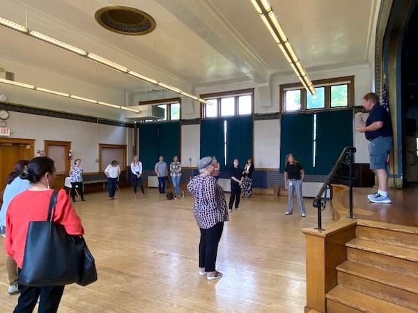 Man communicating from stage in auditorium to a dozen or so people standing on auditorium floor