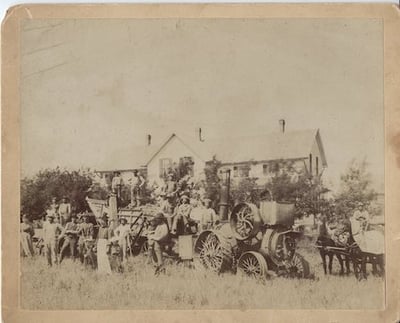 Black and white photo of a THRESHING CREW and equipment in front of farm house