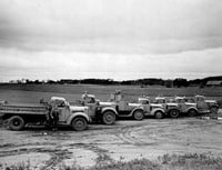 Black and white photograph of highway trucks delivering grasshopper poison to farmers, 1938.