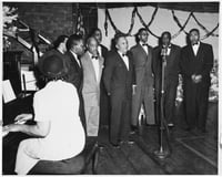 The Wheatley Aires, a men’s singing group, sing in front of an audience at Phyllis Wheatley Community Center (809 Aldrich Avenue North) with a pianist accompanying. ca. 1950.