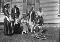 Black and white photograph of Sinclair Lewis and friends, ca. 1916. Lewis sits in the rocking chair at right his wife, Grace Hegger Lewis, wears a maid’s uniform and stands at left.