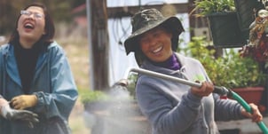 A smiling woman sprays a garden with a hose.