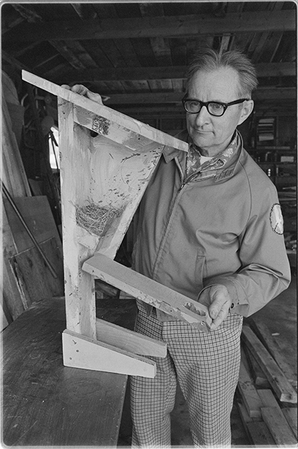 A man stands to show off the inside of a nesting box for birds, revealing the next inside.