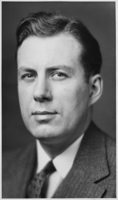 Black-and-white photograph of a man's head and shoulders. He wears a dress shirt, jacket, and tie.
