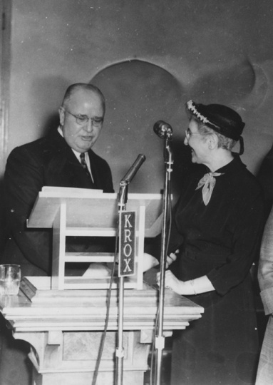 Black and white photograph of Minnesota Supreme Court Justice Roger L. Dell presenting Crookston BPW member Mae Rideout with a “book of golden deeds” in St. Paul, April 12, 1954.
