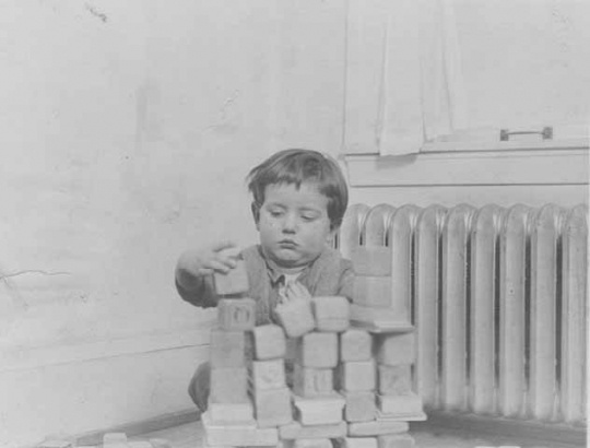Black and white photograph of a toddler playing with blocks at the Northeast Neighborhood House, c.1925.